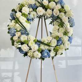 Large floral wreath on a wooden easel with white, blue, and green blooms