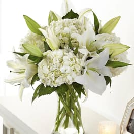 White lilies and hydrangeas arranged in a clear glass vase