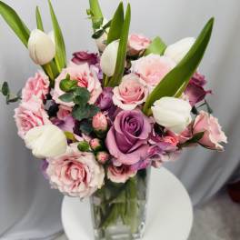 Pink and purple roses with white tulips in a clear glass vase
