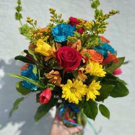 Handheld bouquet of mixed bright flowers in a glass vase