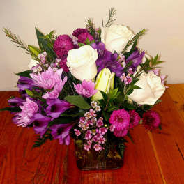 Bouquet of white roses, purple flowers, and pink blooms in a glass vase