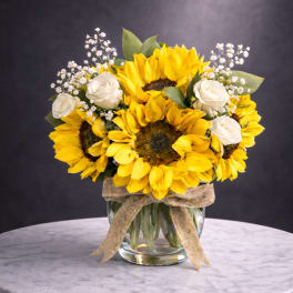 Sunflower and white rose bouquet in a glass vase with a burlap ribbon