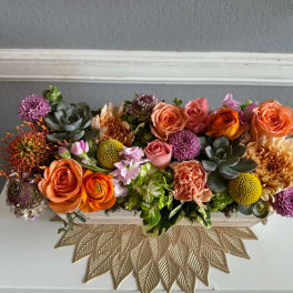Low rectangular arrangement of orange and pink flowers with succulents