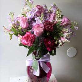 Pink and purple bouquet in a magenta glass vase with a lavender ribbon