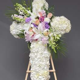White floral cross arrangement with lilies, roses, and hydrangeas on an easel