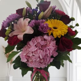 Mixed bouquet of pink, red, purple, and yellow flowers in a glass vase