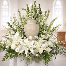 White floral arrangement with lilies and roses around a urn in a church setting