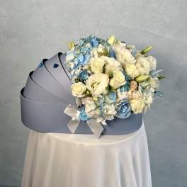 Light blue cradle-shaped box filled with white and blue flowers and a small baby figurine.