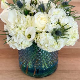 White roses and hydrangeas in a blue glass vase with spiky blue thistles