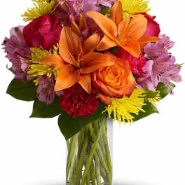 Mixed bouquet of orange lilies, roses, and pink flowers in a glass vase