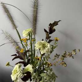 Tall floral arrangement with pale green blooms and feathery grasses in a white vase