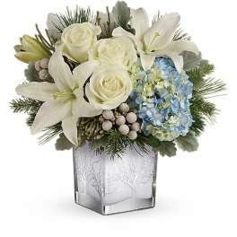 White lilies and roses arranged with blue hydrangea in a frosted glass vase
