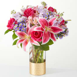 Pink lilies and roses in a clear vase with a gold base