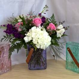 Pink and white flower arrangement in a purple glass vase with two matching gift bags