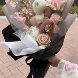 Hand-tied bouquet of pink roses, white ranunculus, and an orchid wrapped in black and white paper