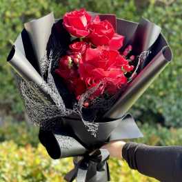 Hand-held bouquet of bright red roses wrapped in matte black paper with black mesh accents