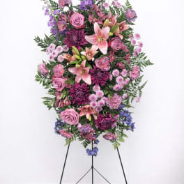 Standing floral spray with pink and purple flowers on a black easel