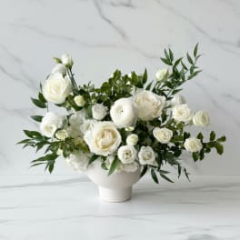 Low white arrangement of ivory roses and ranunculus in a white ceramic bowl