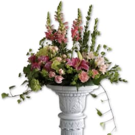 Tall pink and green mixed flower arrangement on an ornate white pedestal column