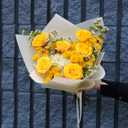 Bouquet of yellow roses and small white flowers wrapped in white paper
