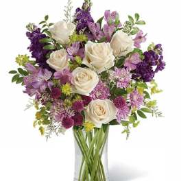 Bouquet of white roses and purple flowers in a clear glass vase