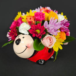 Playful mixed flower arrangement in a red ceramic ladybug container