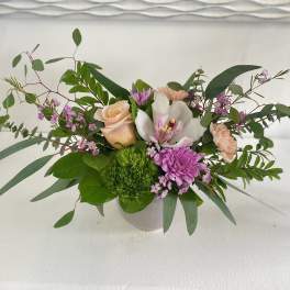 Mixed floral arrangement in a white vase with roses, orchids, and purple blooms