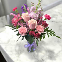 Pink and purple mixed bouquet in a glass vase with a lavender ribbon