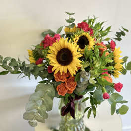 Bouquet of sunflowers, orange roses, and pink carnations in a glass vase