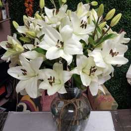 White lilies arranged in a glass vase with a twine tie