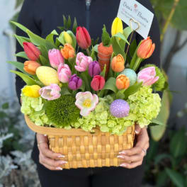 Wicker basket filled with colorful tulips, green hydrangeas, and pastel decorative eggs.