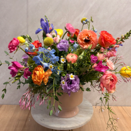 Colorful mixed flower arrangement in a blush ceramic vase on a marble stand