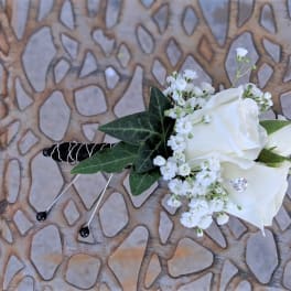 White rose boutonniere with baby's breath and dark green leaves