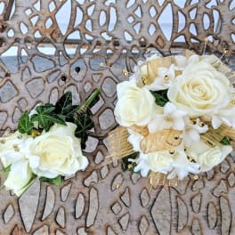 Two white floral corsages with gold ribbon and bead accents
