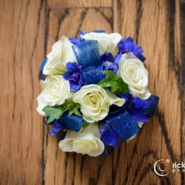 White roses with blue ribbon and purple flowers on a wooden surface