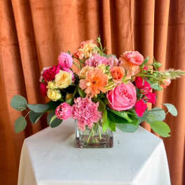 Mixed pink and peach flower arrangement in a square glass vase