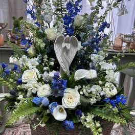 Tall blue and white flower arrangement with an angel figurine in a wicker basket