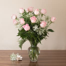 Tall bouquet of light pink roses and white filler flowers in a clear glass vase