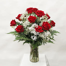 Tall arrangement of red roses and white filler flowers in a clear glass vase