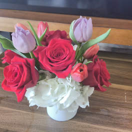 Short arrangement of red roses, tulips, and white hydrangeas in a white vase