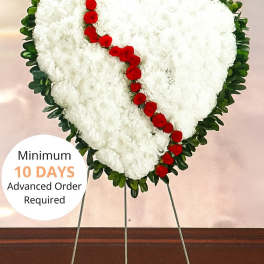 Heart-shaped white funeral wreath with red flowers on a metal stand