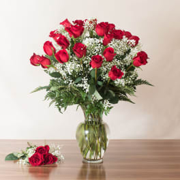 Tall vase of red roses with white filler flowers and a small matching rose bundle on the table