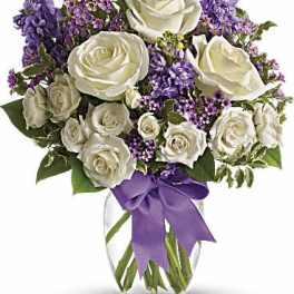 White rose and purple flower arrangement in a clear glass vase with a purple bow