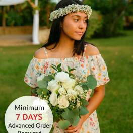 Young woman outdoors holding a white rose bouquet and wearing a white flower crown
