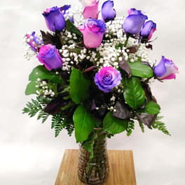 Tall bouquet of pink and purple roses with white filler flowers in a clear glass vase
