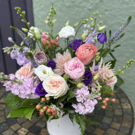 Pastel pink and white flower arrangement with purple accents in a white vase on a mosaic table.