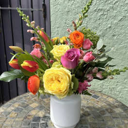 Bright arrangement of yellow roses, pink blooms, and orange tulips in a white vase on a mosaic table