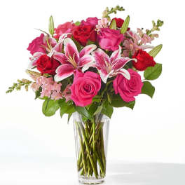 Tall bouquet of pink lilies and red and pink roses in a clear glass vase