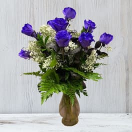 Arrangement of vivid purple roses with white filler flowers in a brown glass vase