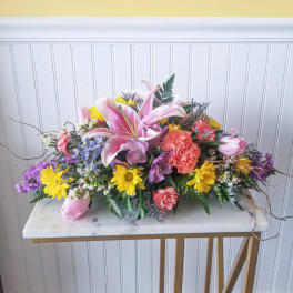 Low centerpiece of pink lilies, carnations, tulips, and yellow daisies in a colorful mixed arrangement